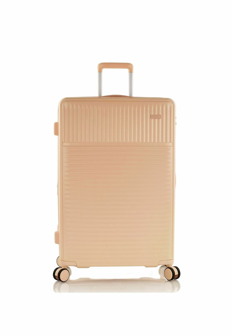 Valise rigide de couleur pêche clair avec une texture à rainures verticales. Équipée d'une poignée télescopique et de quatre roues noires et dorées pour la mobilité.