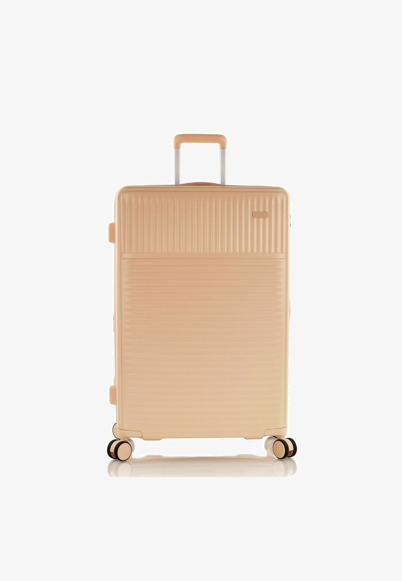 Valise rigide de couleur pêche clair avec une texture à rainures verticales. Équipée d'une poignée télescopique et de quatre roues noires et dorées pour la mobilité.