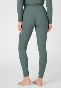 Pantalones de loungewear de color verde con un diseño ajustado. Presentan una pretina ancha y puños en los tobillos ligeramente ajustados. Textura suave, con un detalle mínimo.