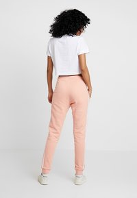 Rosa sweatpants med vita sidostråkar och fickor, kombinerat med en kortärmad vit t-shirt. Tyget verkar mjukt och bekvämt.
