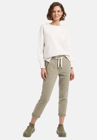 Helle rosa Sweatshirt mit einem runden Ausschnitt, kombiniert mit hellgrünen, tapered Hosen mit verstellbarem Kordelzug. Olivgrüne Schuhe runden den Look ab.