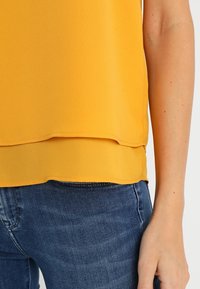 Geel lichtgewicht blouse met gelaagde zoomdetails, gemaakt van een gladde stof. Gecombineerd met blauwe denim jeans, wat een casual stijl toont.