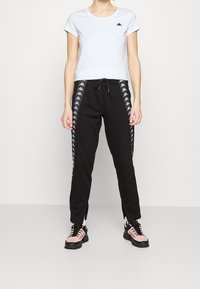 Světle modré tričko s krátkým rukávem a malým logem a černé tepláky s bočním designem v bílé barvě. Tepláky mají zipy na kotnících.