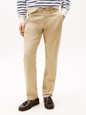 Beige chinos with a smooth texture, featuring a front closure, side pockets, and a slim fit, paired with dark brown loafers.