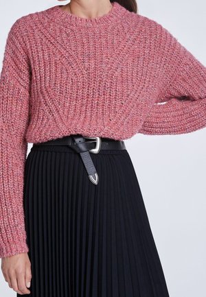 Pull en tricot rose avec un motif texturé, décolleté rond et manches longues, associé à une jupe plissée noire et une ceinture en cuir noir.