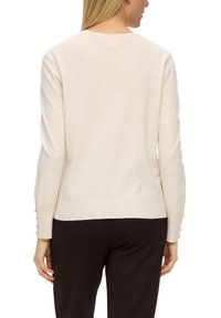 Beiger Pullover mit Rundhalsausschnitt und langen Ärmeln, die an den Bündchen mit Knopfakzenten versehen sind. Der Stoff wirkt weich mit einer glatten Textur.