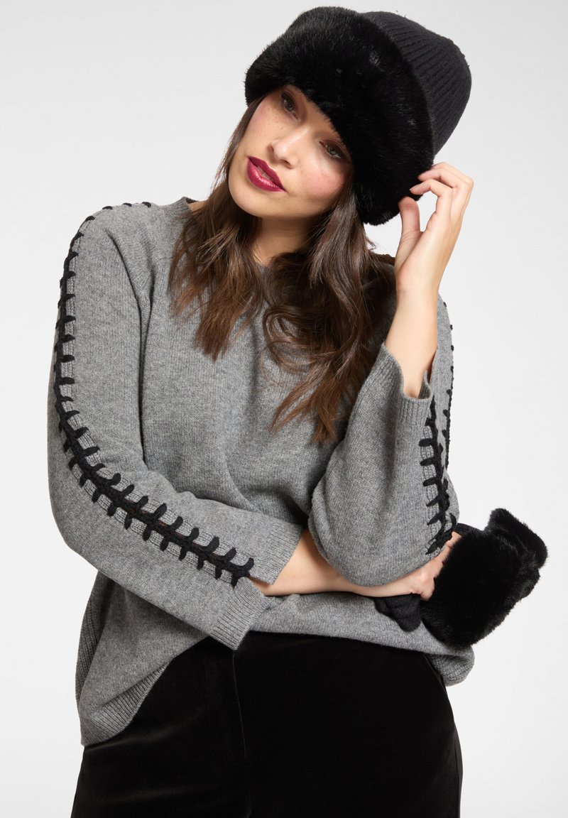 Grauer Strickpullover mit schwarzer Ziernaht entlang der Ärmel; kombiniert mit einem schwarzen Kunstpelzhut und passenden schwarzen Bündchen.