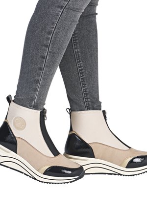 Bottes chevilles beiges et noires au design ressemblant à des chaussettes, avec un bout en vernis et des accents en daim texturé, dotées d'une fermeture éclair sur le côté.