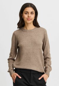 Brązowy sweter dzianinowy z okrągłym dekoltem i długimi rękawami, o miękkiej fakturze i luźnym kroju, w zestawie z czarnymi spodniami.
