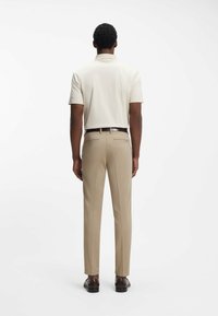 Beige poloshirt en lichtbruine pantalon. Zachte stof met een relaxte pasvorm. Bruine schoenen, strakke lijnen en geen zichtbare patronen of details.