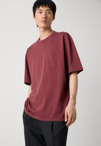 Μπορντό κοντομάνικο t-shirt από μαλακό βαμβάκι με τσέπη στο στήθος. Διαθέτει διακριτές ραφές και άνετη εφαρμογή.