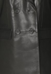 Manteau noir en cuir à double boutonnage avec une texture lisse, comprenant deux grands boutons ronds et des poches latérales. Design ajusté avec des revers nets.