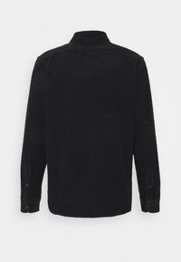 Camisa de pana negra con cuello, mangas largas y puños abotonados. Presenta una textura de rayas verticales en toda la tela.