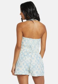 Ljusblå mönstrad jumpsuit med smockad bodice, halterneck och löst sittande shorts med geometrisk design.