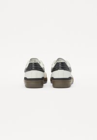 Sneaker bianche e nere con suola in gomma testurizzata, dotate di tallone imbottito e sovrapposizioni a contrasto. Design pulito senza loghi visibili.