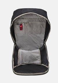 Interior de mochila negra con forro gris, que cuenta con múltiples bolsillos, incluyendo un bolsillo de malla y una sección plana en la parte inferior.