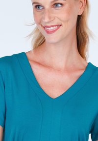 Teal-farbenes V-Ausschnittoberteil mit kurzen Ärmeln, glatter Textur und dezenten Steppnähten entlang des Ausschnitts. Geeignet für die Freizeit.