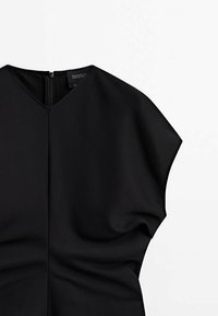 Robe noire avec un col en V, des manches courtes larges et une fermeture éclair au dos, posée à plat sur un fond blanc.