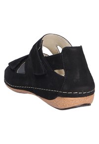 Zwarte suède schoen met een lage kurken hak, voorzien van een uitsnijdontwerp en klittenbandriemen voor gemakkelijk aan- en uittrekken. Stevige, gestructureerde bovenkant met gestikte accenten.