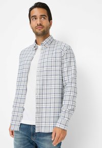 Langsleeve geruit shirt in lichtgrijs met blauwe en witte strepen, met een button-down kraag en zachte stof. Draagt over een wit T-shirt.