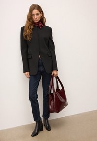 Juodas pritaikytas švarkas su aštriais pečiais, derinamas su tamsiai mėlynomis džinsomis ir juodomis kulkšninių botais. Laiko blizgų bordo spalvos petinį krepšį.