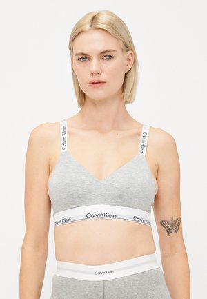 Bralette grigio con design a V, caratterizzato da un elastico bianco con il marchio "Calvin Klein". Spalline regolabili e texture morbida.