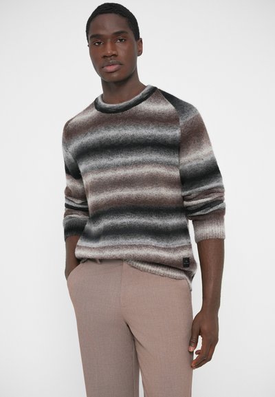 Πλεκτό πουλόβερ με εναλλασσόμενες ρίγες σε αποχρώσεις του καφέ, γκρι και μαύρου, με στρογγυλή λαιμόκοψη και ριμπ μανσέτες. Ζευγάρι μπεζ παντελόνια.