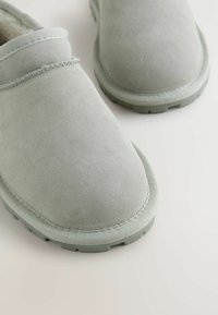 Jasnoszare zamszowe buty wsuwane z okrągłym noskiem, teksturowaną cholewką i gumową podeszwą; mają prosty, przeszywany wzór i brak widocznych elementów metalowych.