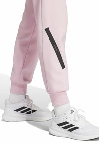 Ljust rosa joggers med en svart sidremsa och textdetalj, i kombination med vita sneakers med tre svarta ränder och texturerade sulor.