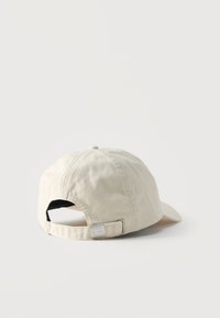 Μπεζ βαμβακερό καπέλο μπέιζμπολ, εμφανιζόμενο από πίσω, με ρυθμιζόμενο λουρί με μεταλλικό αγκράφα σε απλό λευκό φόντο.