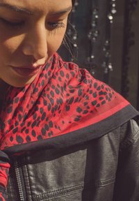 Red and black leopard print scarf draped over a black leather jacket, featuring a smooth texture and contrasting solid borders.