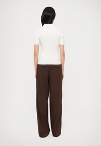 Biely priliehavý rebrovaný top s krátkymi rukávmi, skombinovaný s voľnými hnedými nohavicami s vysokým pásom; hladké textúry a čisté línie.