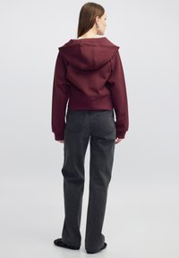 Sudadera corta color burdeos con una gran capucha, puños acanalados y costuras en la parte posterior. Combinada con jeans de pierna ancha gris oscuro y bailarinas negras con adornos.