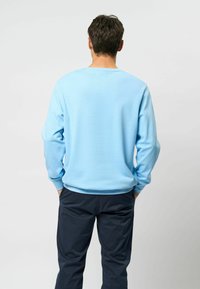 Vaaleansininen pitkähiha sweater pyöreällä pääntiellä, resorikätköillä ja sileällä tekstuurilla. Päällä tummien housujen päällä, rento istuvuus.