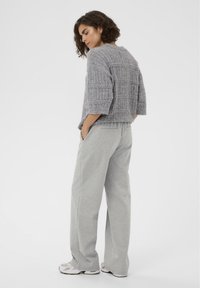 Hall halli kampsun tekstuurse mustriga, kombineeritud heledate hallide dressipükste ja valgete tossudega, vaadatuna tagantpoolt.