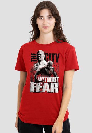 Woman wearing a red T-shirt with black and white graphic of two men and text "The City Without Fear."