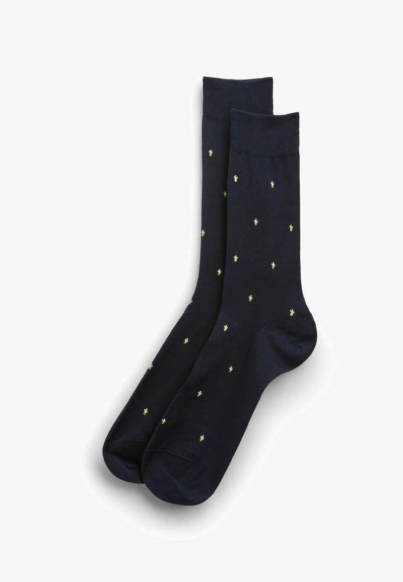 Paire de chaussettes noires avec de petits motifs de cactus verts répartis uniformément sur le tissu, présentées sur un fond blanc.