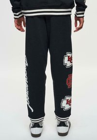 Svarta sweatsbyxor med vita logotyper och text. Har en avslappnad passform, ribbade fållar och ränder vid midjan. Matchas med vita sportskor.