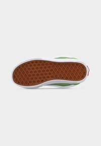 Σόλα αθλητικού παπουτσιού με καφέ υφή τύπου βαφλά, λευκή ενδιάμεση σόλα και εμφανή πράσινο πάνω μέρος σε λευκό φόντο.