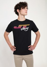 Černé bavlněné tričko s logem "JT Racing" v růžových a žlutých pruhem. Krátké rukávy, kulatý výstřih a volný střih.