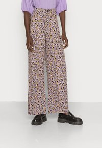 Calças largas florais com um padrão roxo, amarelo e preto, apresentando uma cintura alta e um corte descontraído, acompanhadas de sapatos plataforma pretos.