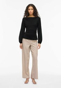 Czarna teksturowana bluzka z długim rękawem i kwadratowym dekoltem, zestawiona z jasnobeżowymi szerokimi spodniami i metalicznymi sandałami na obcasie.