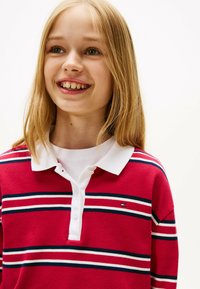Rood gestreept poloshirt met witte kraag, met marineblauwe en witte horizontale strepen. Zachte textuur en knopen bij de hals.