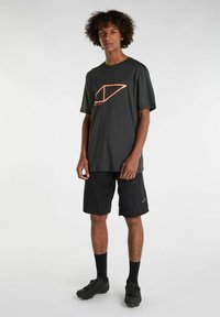 Musta nopeasti kuivuva t-paita, jossa on kontrastiväri oranssi geometrinen logo, yhdistettynä mustiin shortseihin ja mustiin kenkiin, joissa on tekstuuripohjat.