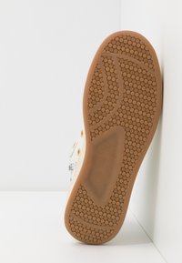Hvide sneakers med gummisål, der har en mønstret, tekstureret bund. Metaløjer og minimale design detaljer på overdelen.