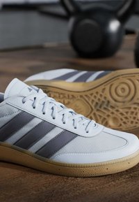 Witte sportieve schoenen met grijze strepen, een gestructureerde bovenkant en een rubberen gumzool. Beschikt over veters en een gedetailleerd patroon op de outsole.