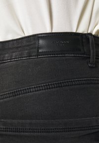 Calças de ganga pretas com uma etiqueta de imitação de pele com "VERO MODA" e detalhes de costura distintos ao longo da cintura.