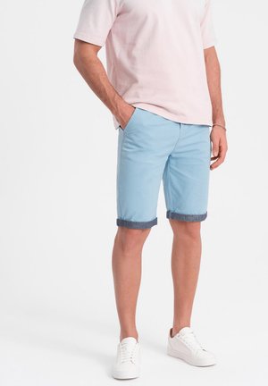Pantaloni corti azzurri con orlo arrotolato e rifiniture in denim scuro, abbinati a una maglietta rosa e scarpe da ginnastica bianche. Stile casual, tessuto intrecciato.