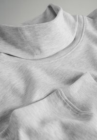 Grauer, Baumwollmischung-Turtleneck-Oberteil mit geripptem Kragen und Bündchen, das eine glatte Textur und einen lässigen Schnitt aufweist. Nahaufnahme des Stoffes.