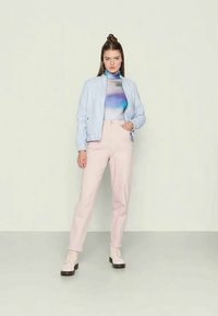 Svetlo modra bomber jakna čez večbarvno srajco, v kombinaciji s svetlo rožnatimi hlačami in bež vezalkami. Gladke teksture, sproščen kroj.